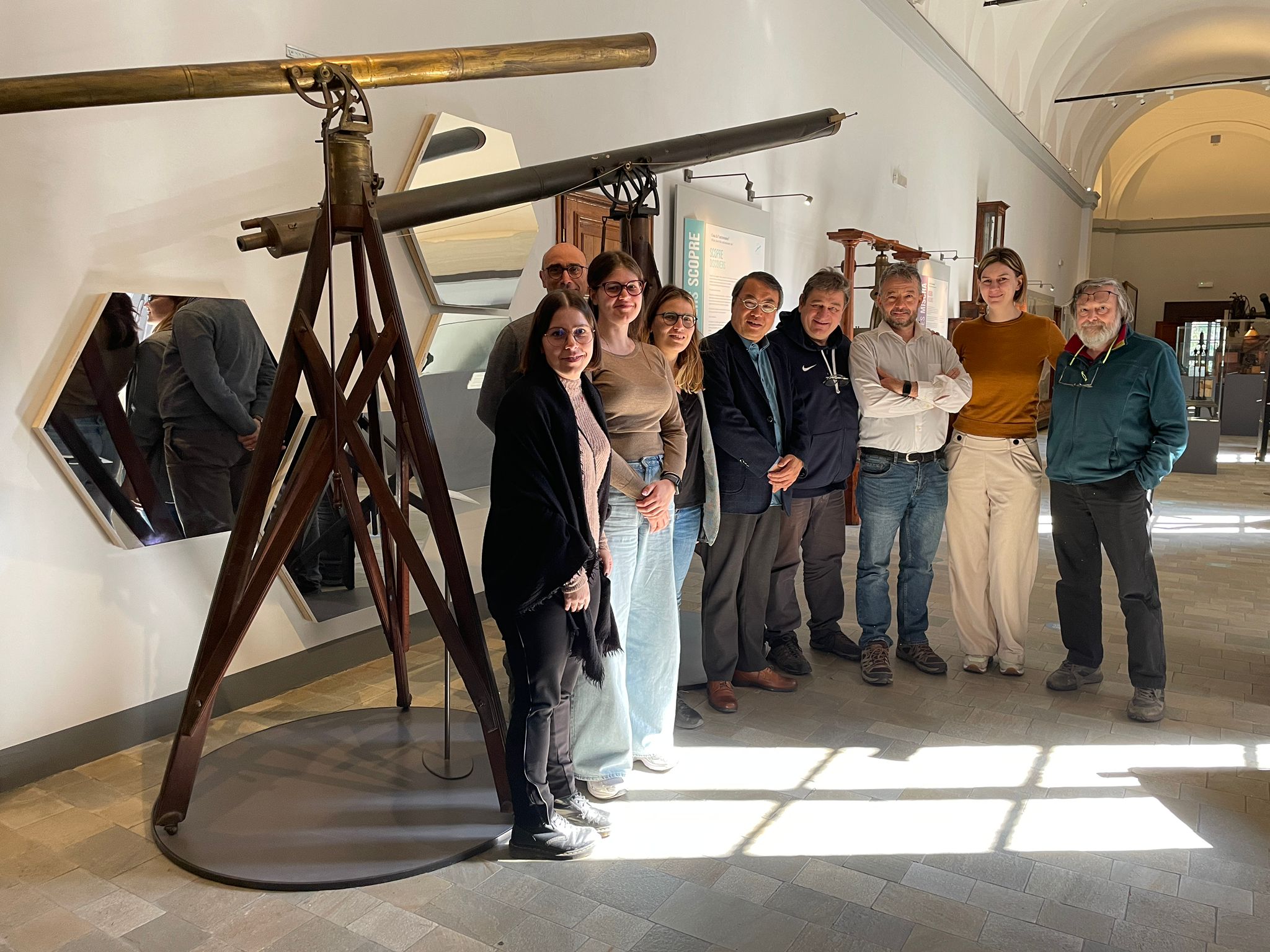 Il Prof. Cao Zhen al Museo Astronomico di Brera insieme ai/alle ricercatori/ricercatrici del team ASTRI Mini-Array (da sinistra: S. Anzuinelli, S. Scuderi, C. Quartiroli, S. Crestan, Prof. Cao Zhen, G. Pareschi, A. Giuliani, M. Rigoselli, S. Vercellone). Sullo sfondo è visibile un’installazione museale realizzata con tasselli di specchio provenienti dai telescopi ASTRI.